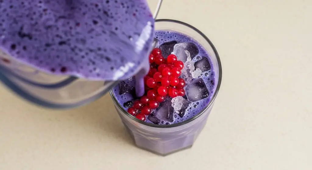 Pouring blended berry frappuccino into glass over pearls